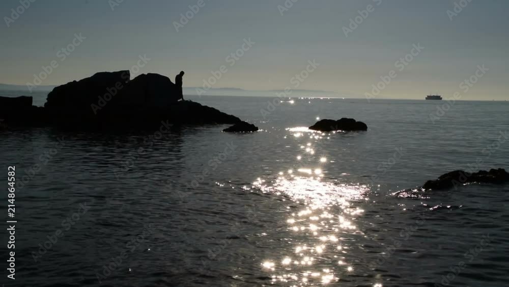 silhouette of men on the rocks in the sea while the cruiser ship sails in the background silhouette of men on the rocks in the sea while the cruiser ship sails in the background