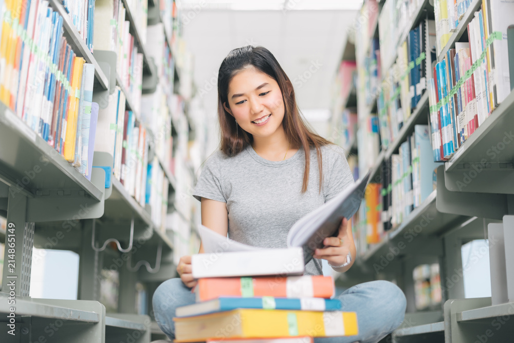 Asian Woman reading and sitting near a bookshelf in the library.. Asian Woman reading and sitting near a bookshelf in the library..