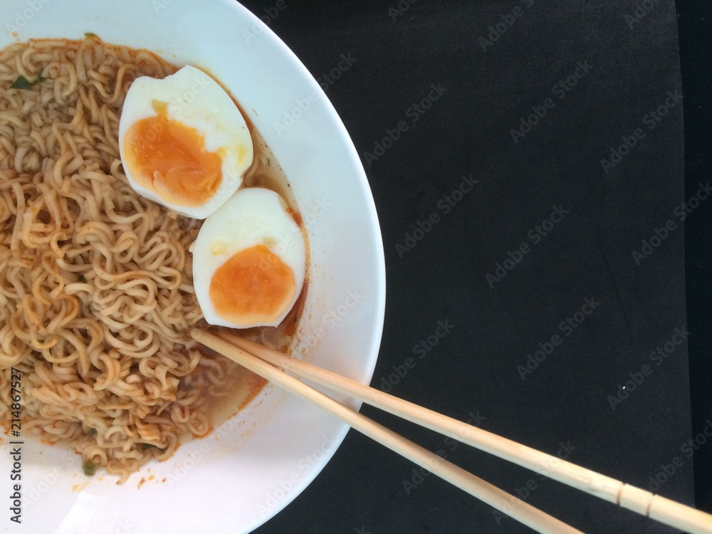Noodles , egg and chopsticks in a white bowl placed on a black table. Noodles , egg and chopsticks in a white bowl placed on a black table.