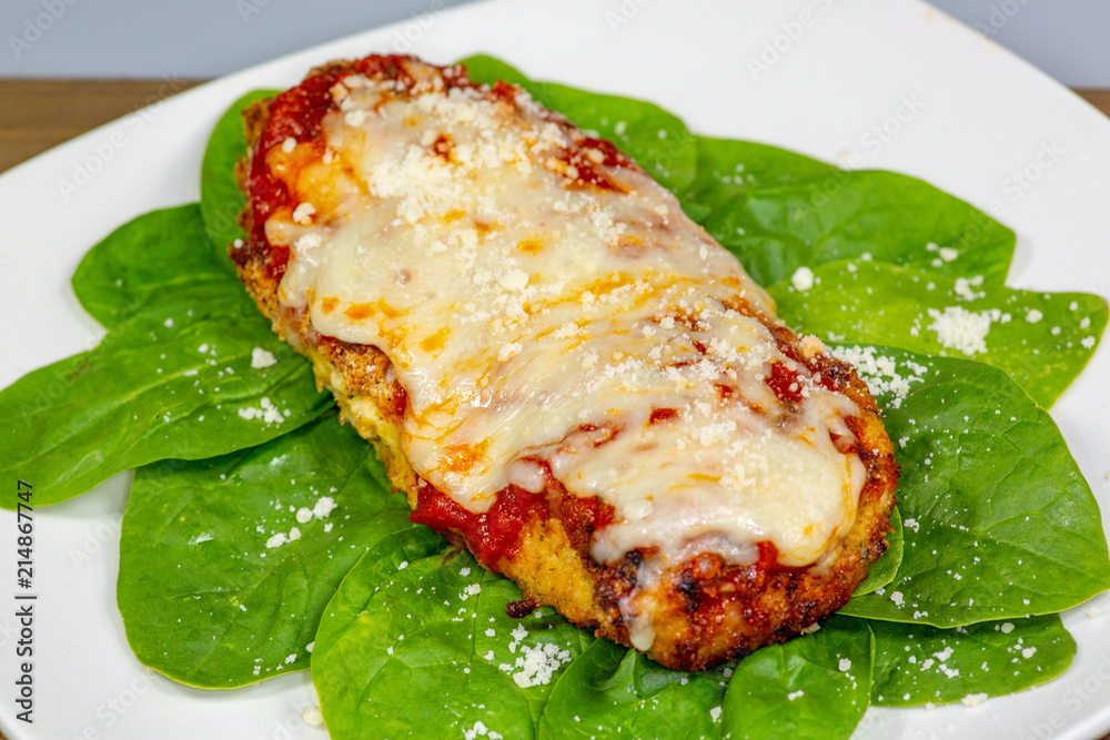 Chicken Parmesan on a bed of spinach with a sprinkle of fresh parmesan cheese on top on a white plate Chicken Parmesan on a bed of spinach with a sprinkle of fresh parmesan cheese on top on a white plate