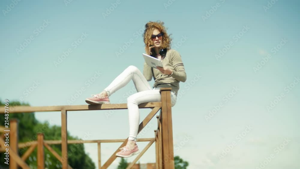 Young beautiful woman sits on the beach in headphones and uses a tablet Young beautiful woman sits on the beach in headphones and uses a tablet