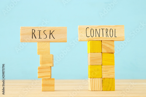 concept image of Wooden cubes that create an unstable structure and the word risk next to steady one with the word control.