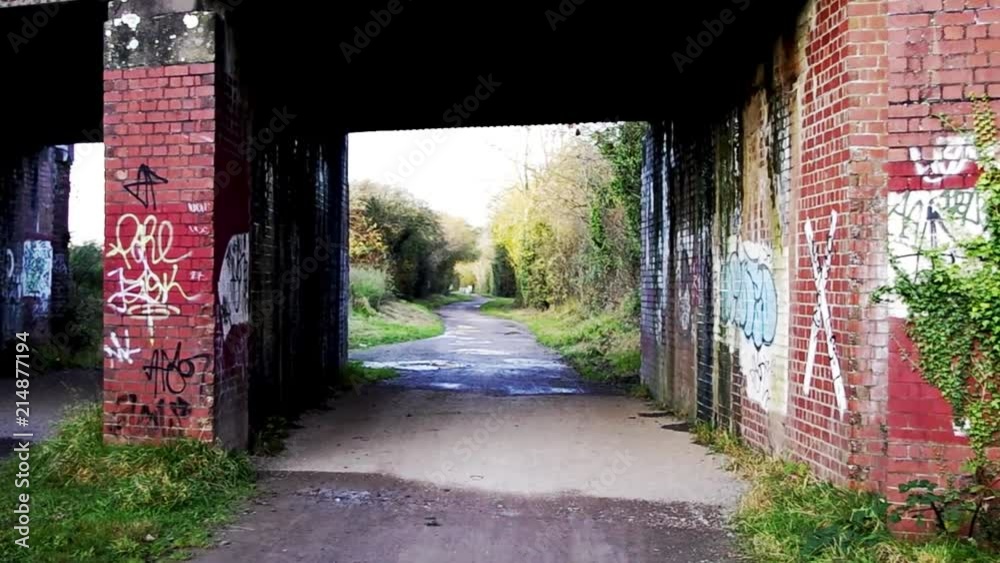 Zoom in of an urban red brick railway bridge on a pathway in Swindon. The bridge has visible graffiti Zoom in of an urban red brick railway bridge on a pathway in Swindon. The bridge has visible graffiti