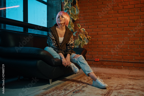 Girl with pink hair sitting relaxed on a leather sofa