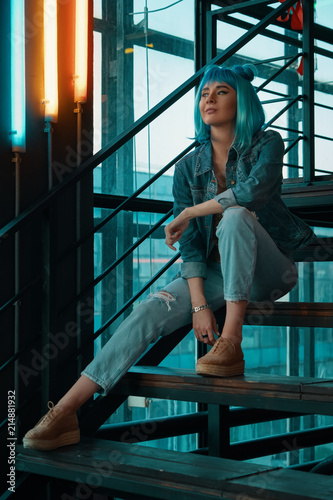  Stylish woman wearing a blue wig sitting on stairs in a modern 