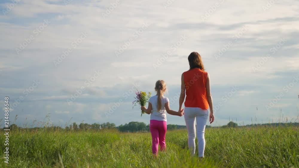 Mom and daughter in a field of flowers. Happy family mother and child daughter have fun on flowers. Cheerful daughter gifts bouquet of flowers to her mother. Mom and daughter in a field of flowers. Happy family mother and child daughter have fun on flowers. Cheerful daughter gifts bouquet of flowers to her mother.