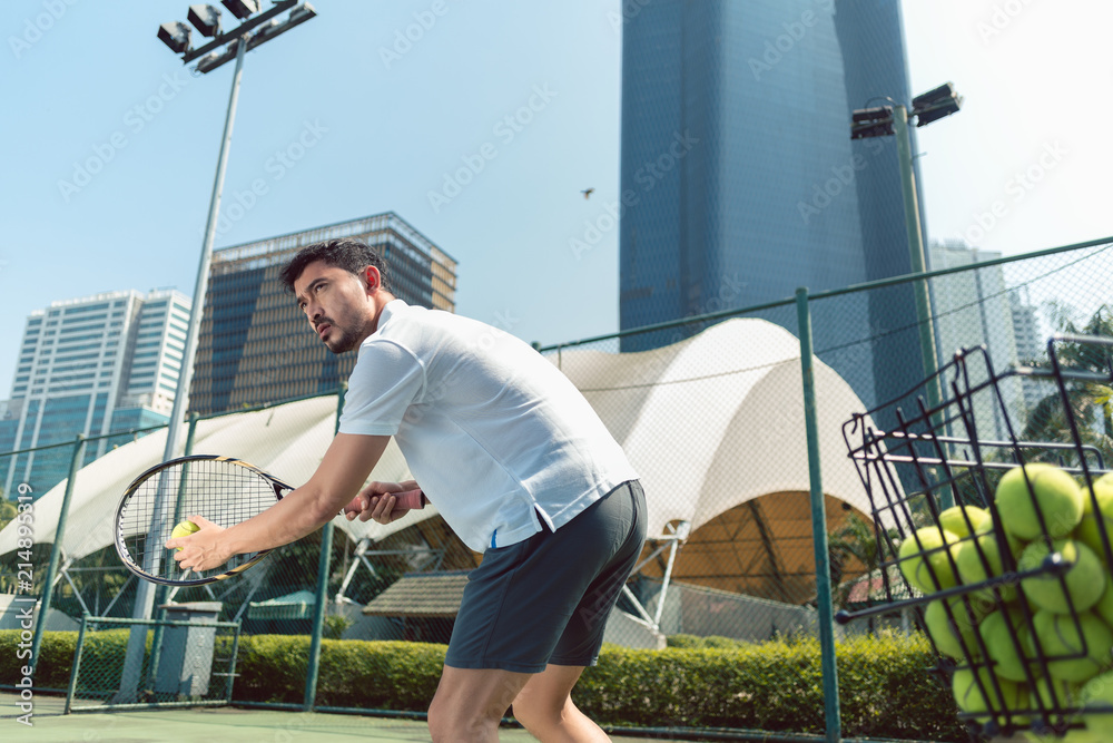 Low-angle view of a young handsome man ready to serve while playing tennis outdoors in a modern district of the city
