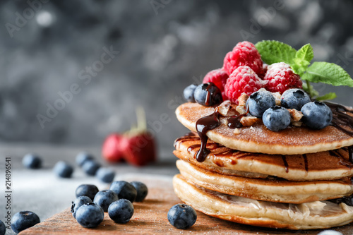 Tasty homemade pancakes with berries on wooden board, closeup photo