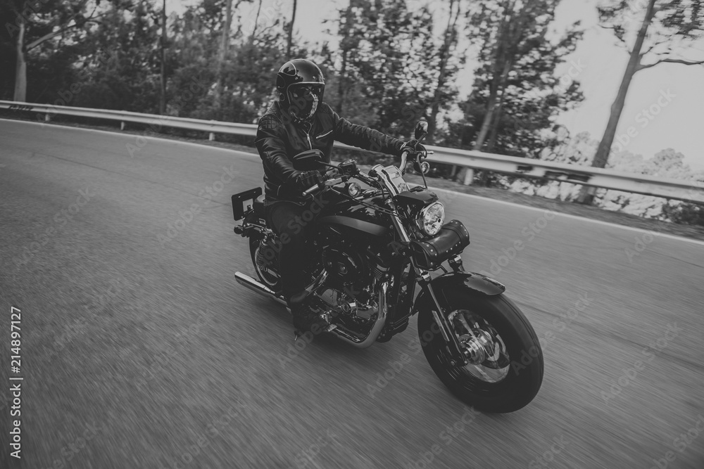 Black and white of man riding a classic motorcycle on the road.
