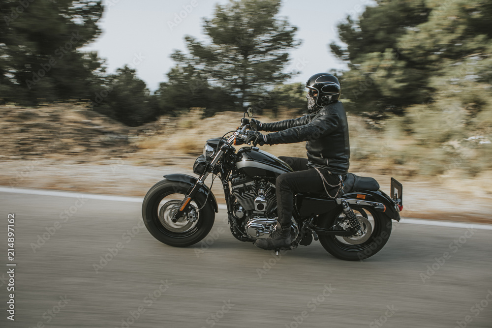 Naklejka premium Mężczyzna w czarnej skórzanej kurtce na motocyklu na drodze przez górę.