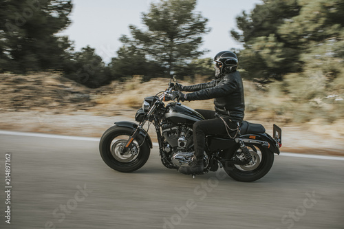 Man in black leather jacket riding a motorcycle on the road across the mountain. photo