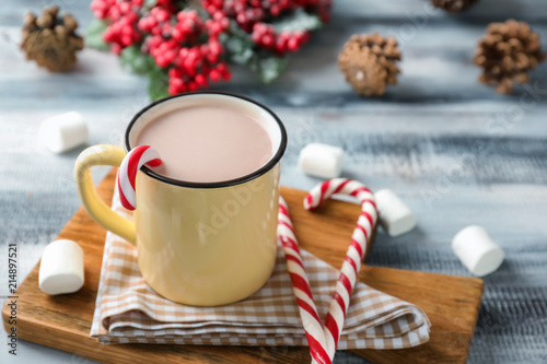 Metal mug of hot cocoa with candy canes on wooden board