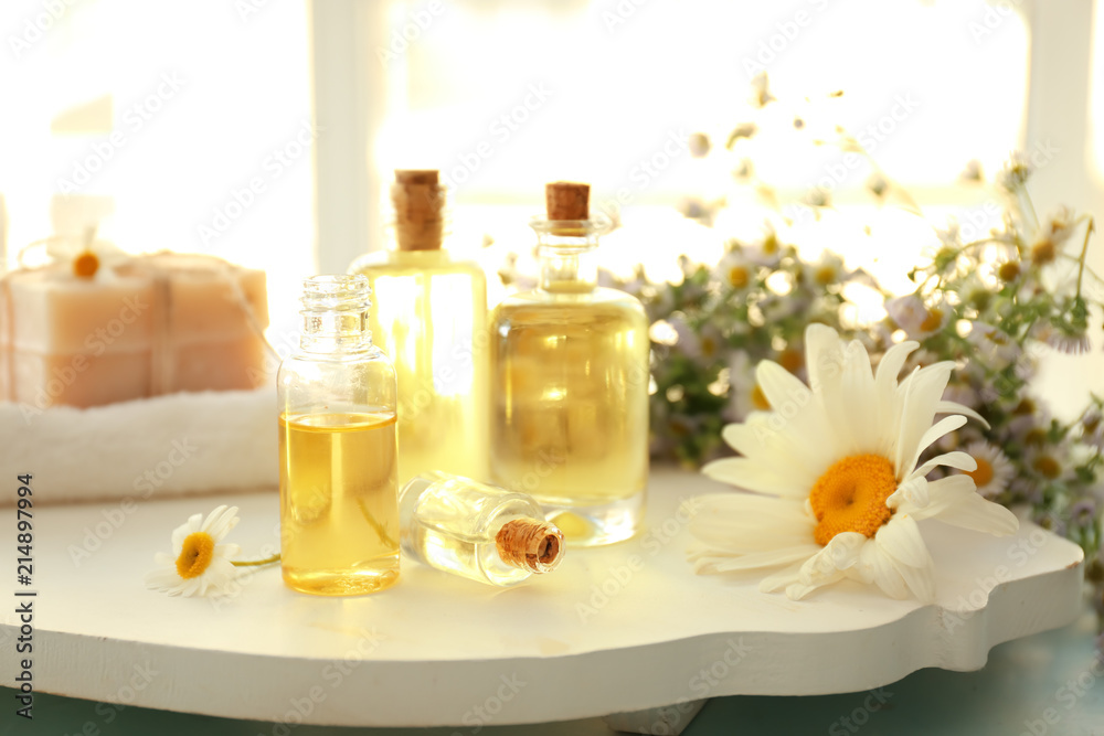 Bottles of essential oil with chamomile flowers on white board Bottles of essential oil with chamomile flowers on white board