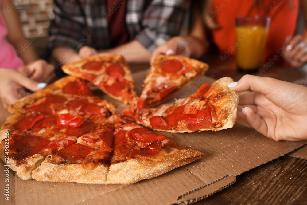 Young people taking slices of delicious pizza from cardboard box on table