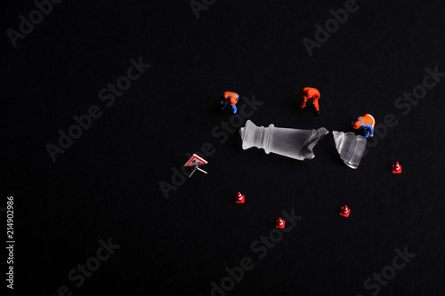A group of miniature figurine workers surrounding a piece of broken chess. Maintenance and workmanship conceptual. photo
