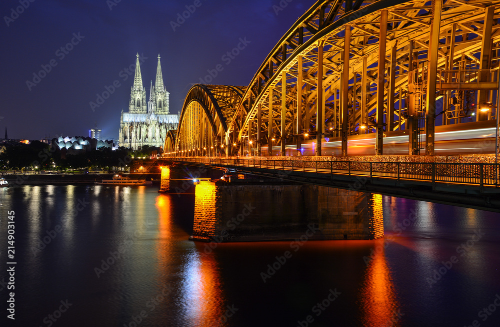 Fototapeta premium Night panorama of Cologne, Germany, with the river Rhine, the railway Hohenzollern Bridge and Cologne Cathedral, a famous landmark and a largest gothic church in Northern Europe