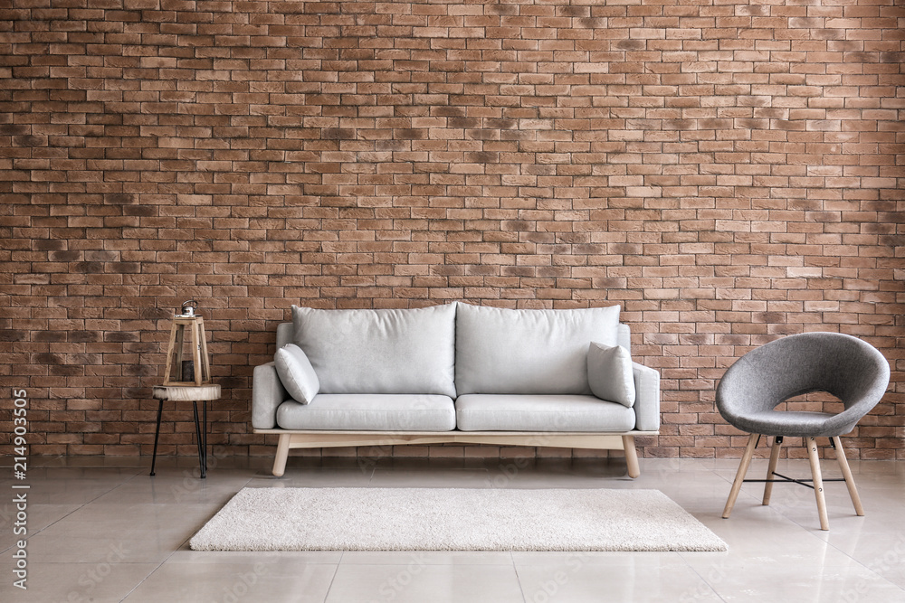 Modern interior of living room with comfortable sofa and armchair near brick wall - obrazy, fototapety, plakaty 