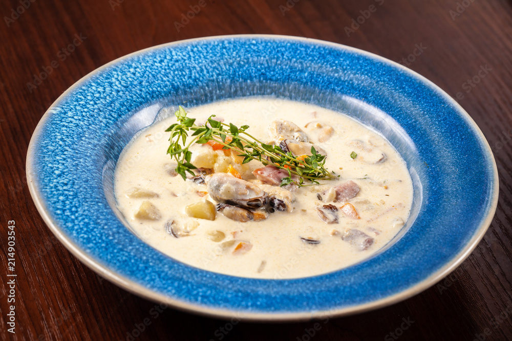 The concept of Italian cuisine. Creamy soup with seafood, mussels, potatoes, carrots, thyme. serve in a blue plate.