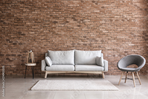 Modern interior of living room with comfortable sofa and armchair near brick wall photo