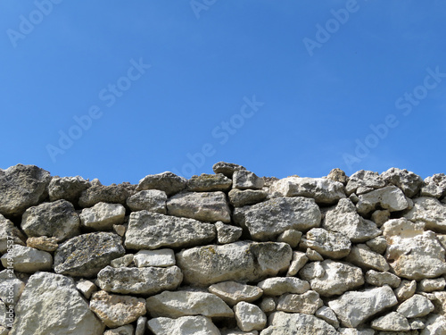 The wall of natural stones on the background of clear blue sky. Ancient limestone masonry 
