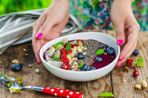 Females hands putting berries into smoothie bowl
