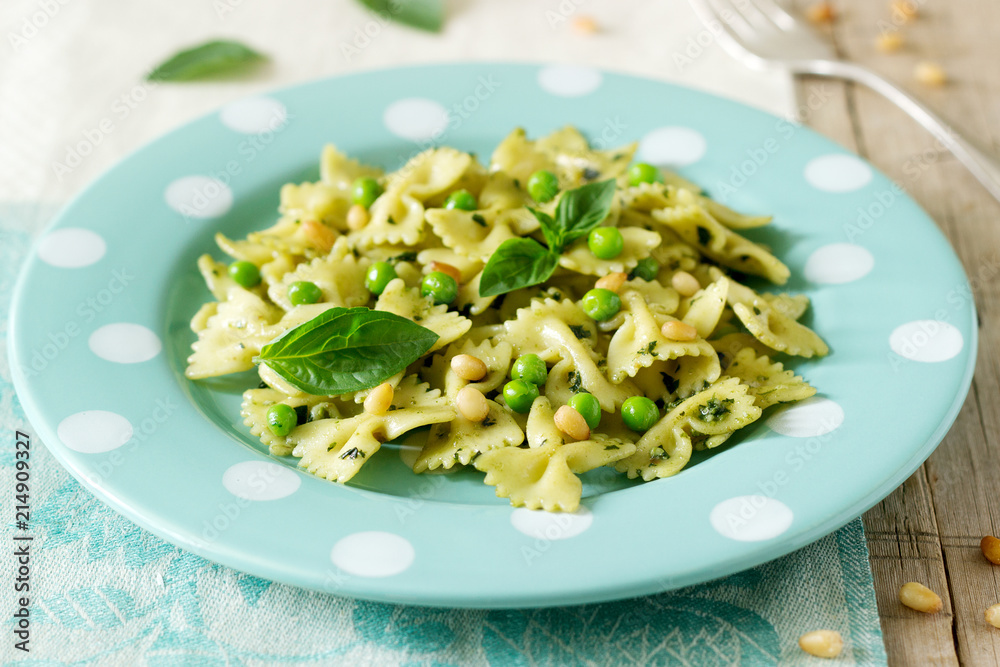 Pasta with pesto sauce, green peas and basil on a wooden table. Rustic style.
