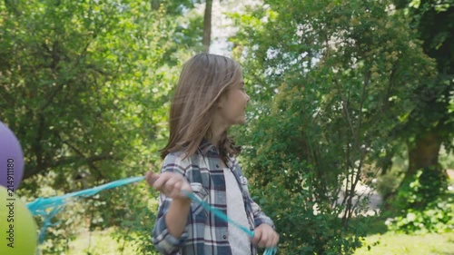 Happy young girl rejoicing with colourful balloons in a park