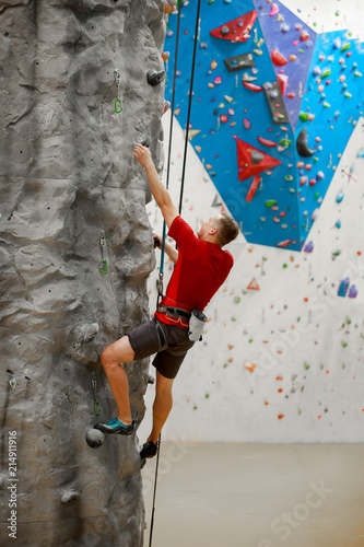 Photo from back of sports male exercising on climbing wall