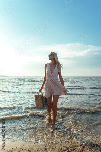 a girl in a fashionable bow with a handbag in her hands comes out of the sea