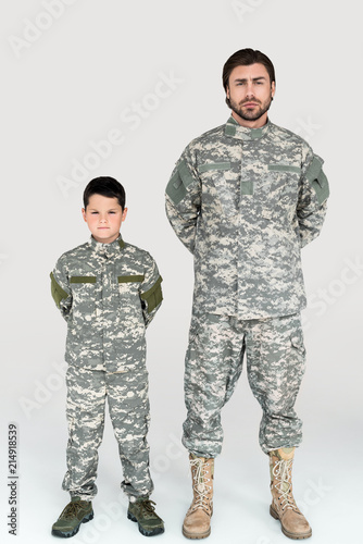 father and son in military uniforms looking at camera on grey background