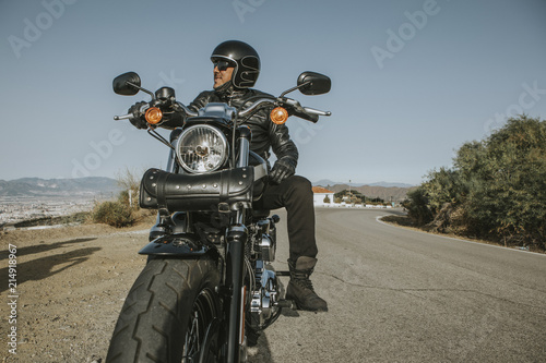 Man with black helmet  jacket and sunglasses standing on a classic American motorcycle.
