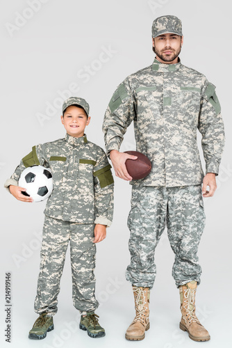 family in military uniforms holding soccer and rugby balls on grey background