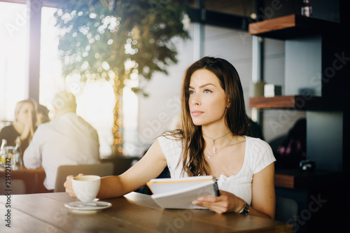 Free Download Portrait of a young, beautiful girl sitting in a cafe, drinking coffee, reading a paper, working, thinking, studying, enjoying. - GFXLoad