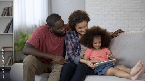 Fotografie Parents watching their little daughter learning educational app on tablet