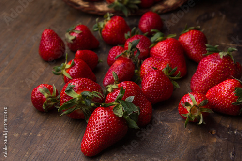 Bunch of red, fresh, washed strawberries on a wooden table spilled from a wooden basket.