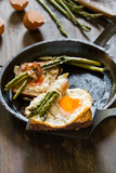 Delicious fried eggs on a toasted bread in a metal pan with grilled asparagus wrapped in fried bacon.