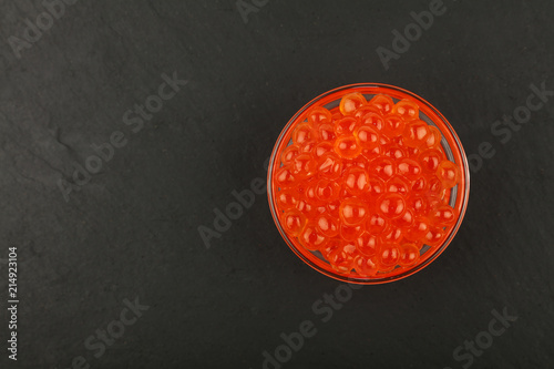 Close up glass bowl of red salmon caviar on black