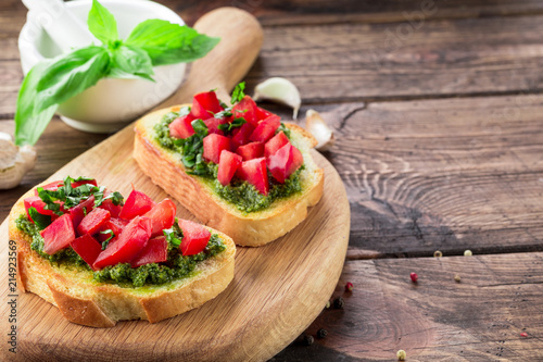 Bruschetta with fresh pesto, basil leaves and tomatoes. Wooden background