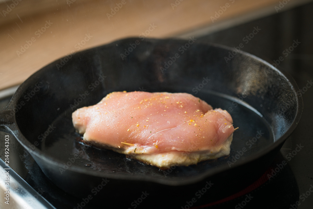 One of the steps in preparation of a raw stuffed chicken breast in a cast-iron pan ; grilling the meat.