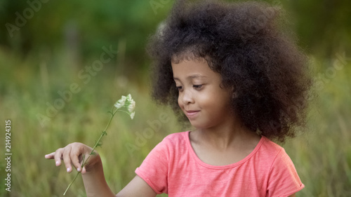 Little lonesome kid standing in garden and playing with small white flower