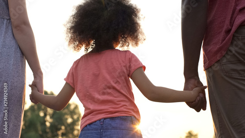 Curly-haired girly holding her mother and father hands, happiness in family photo