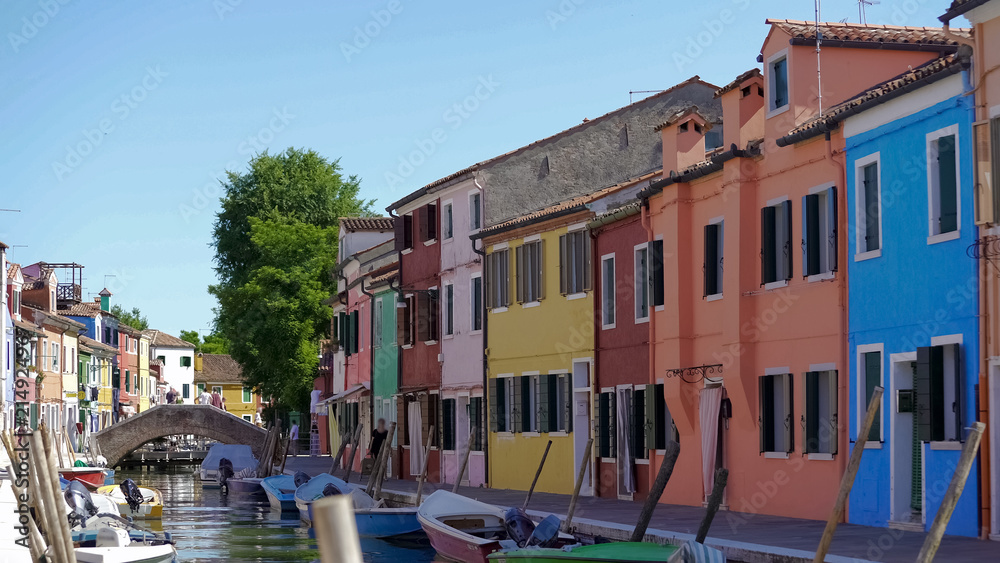 Beautiful street with tidy buildings and boats moored along canal, Burano island