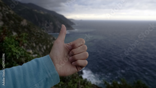 Male hand thumbs up against rocks and sea background, active recreation, tourism