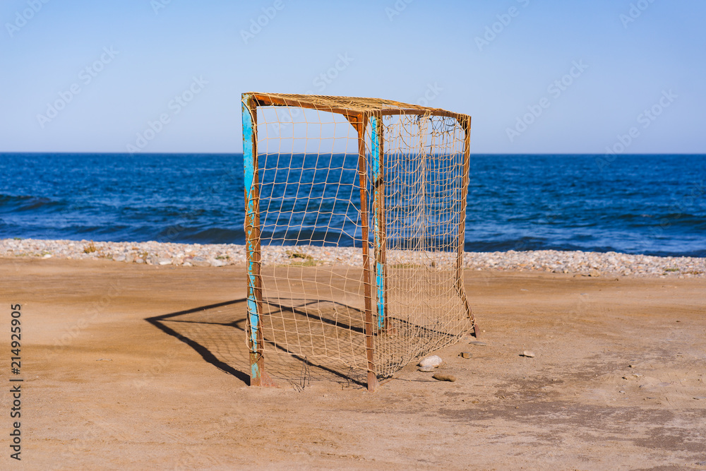 Old vacant football soccer goal gate on front of the blue ocean. Old sports field with rusty goal and net on meadow with muddy front line. Old vacant football soccer goal gate on front of the blue ocean. Old sports field with rusty goal and net on meadow with muddy front line.