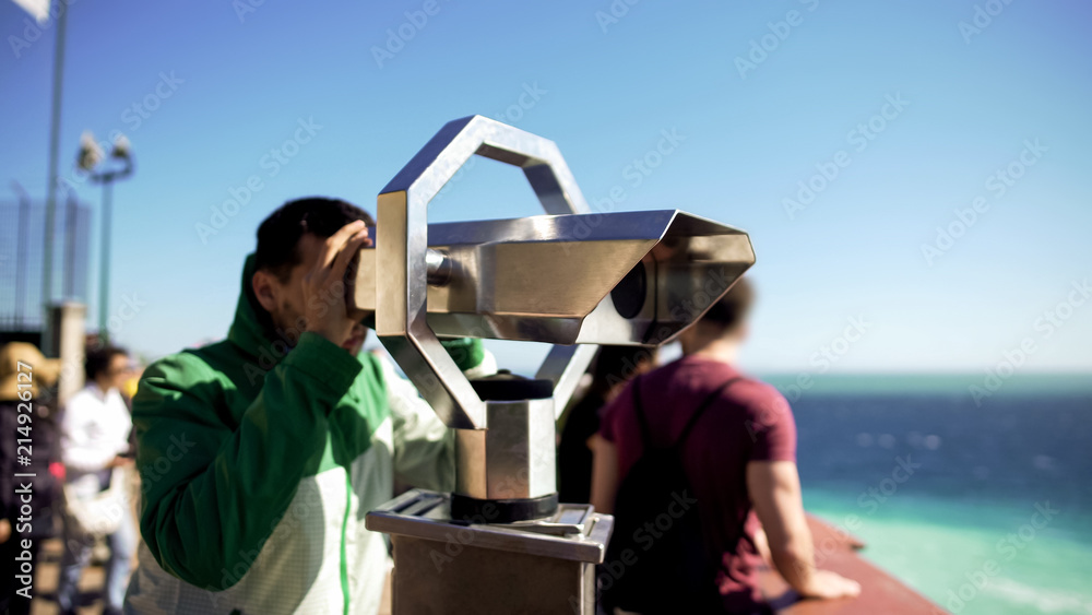 Tourist looking through binoculars at observation deck, man admiring seascape