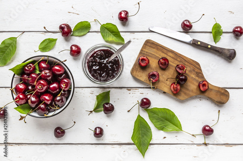 Jar of cherry jam and cherries on white wood