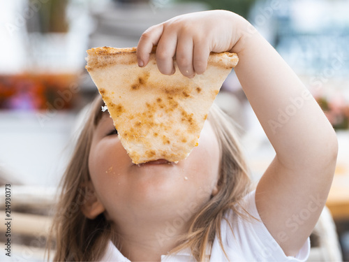 A young girl with plaits is eating a piece of pizza Horizontal