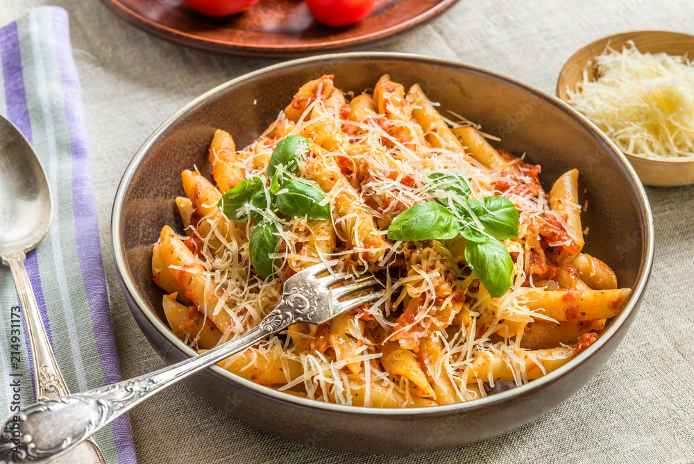 Pasta All'Arrabbiata, penne with tomato sauce and basil and parmesan cheese on a rustic wooden table with linen napkin