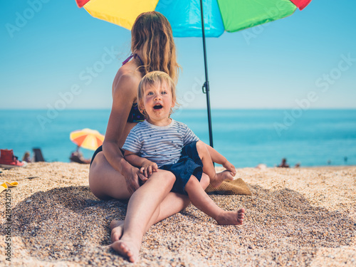 Mother with toddler under parasol on beach