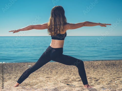 Woman in warrior yoga pose on beach